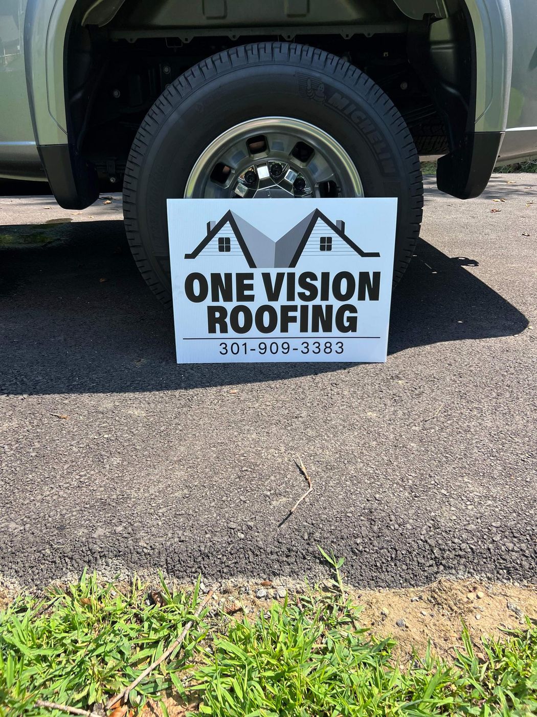 One Vision Roofing yard sign leaning against a truck wheel