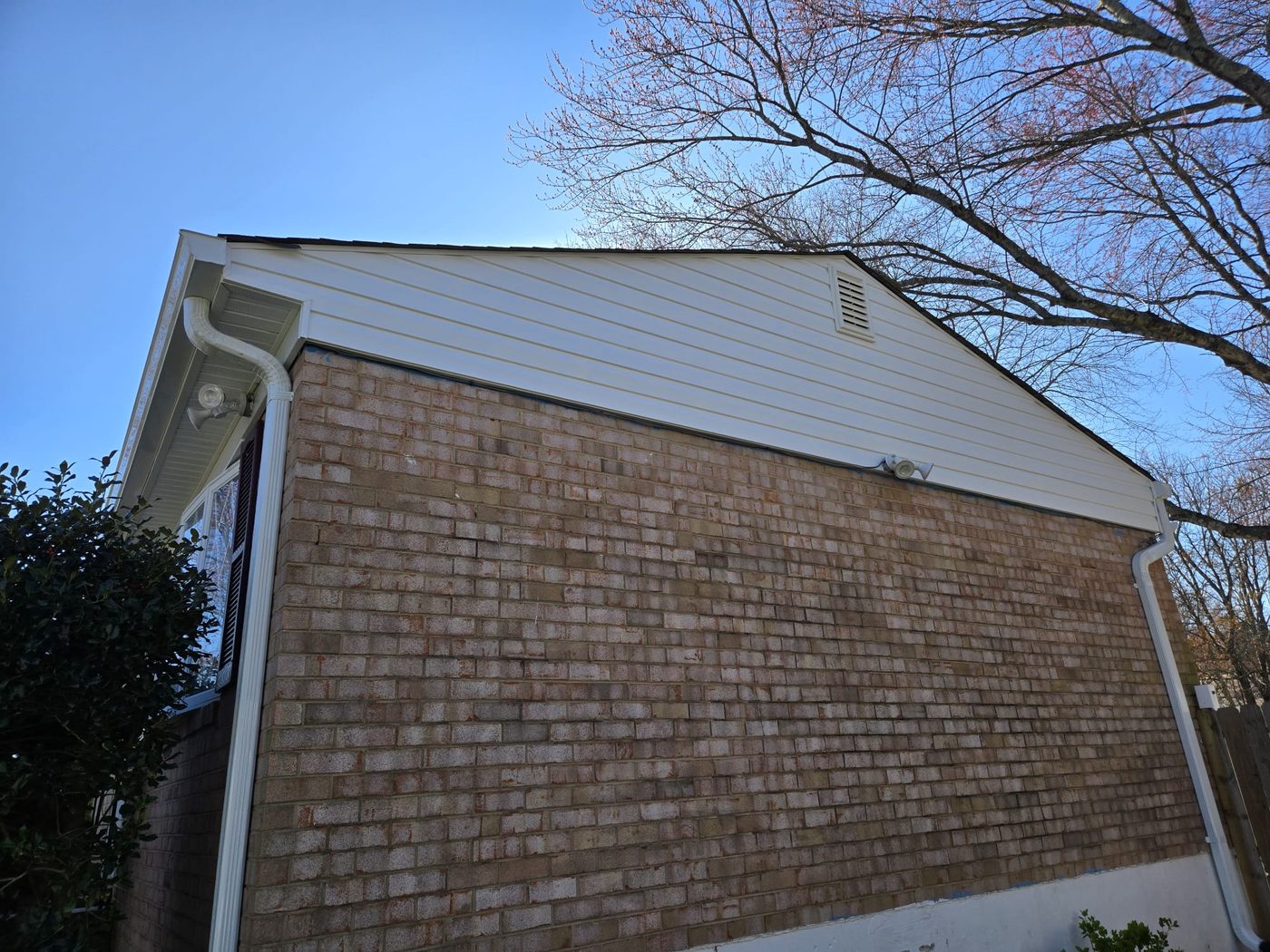 Gutter and downspout on a brick home with a vinyl gable