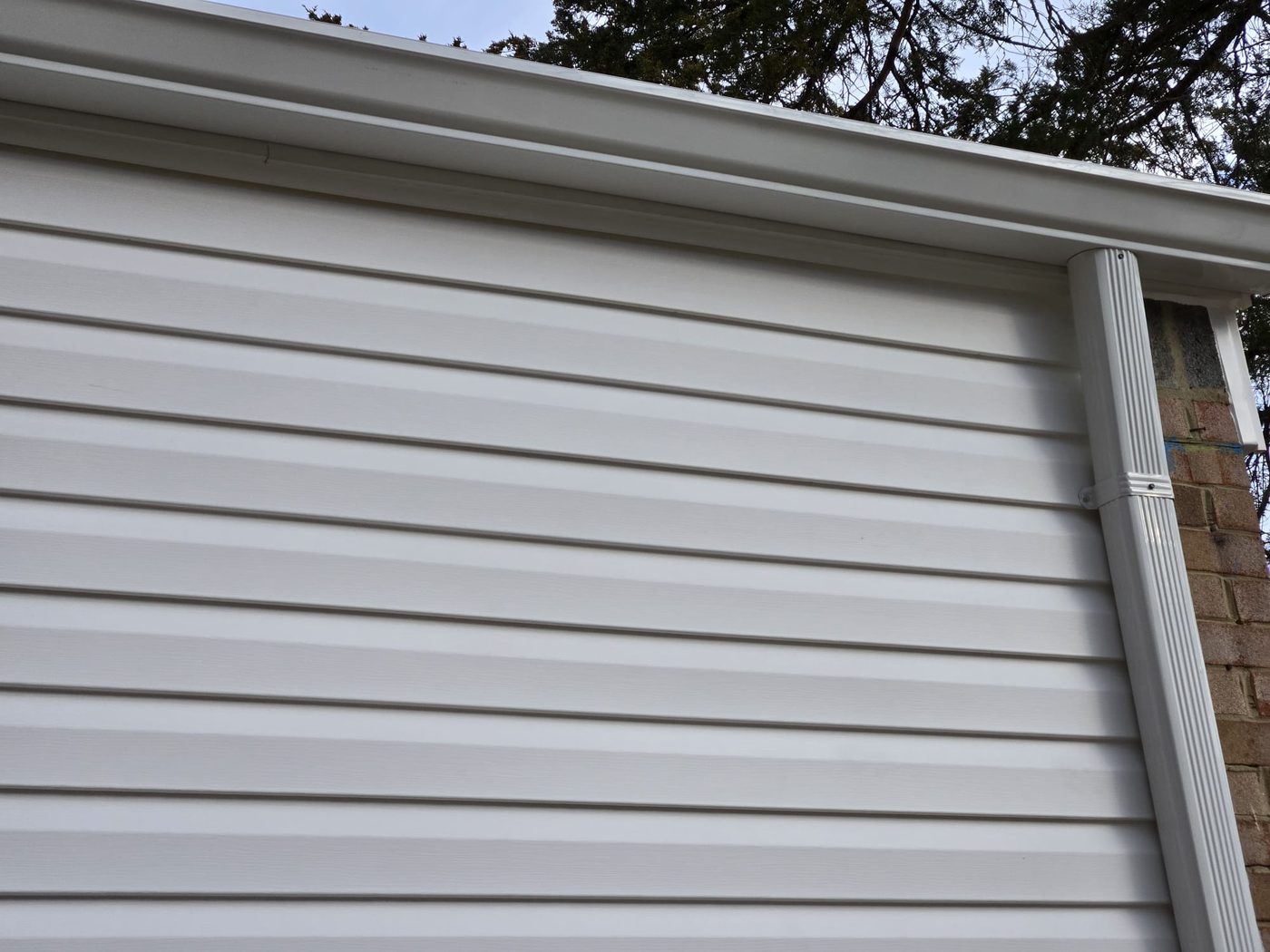 Close-up of a white gutter and downspout along vinyl siding
