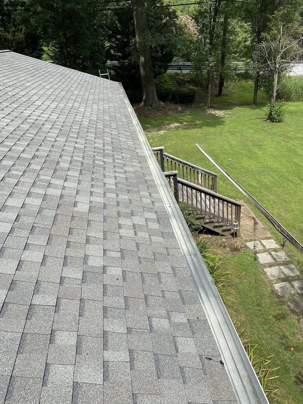Close view of a shingle roof edge and gutter above a backyard