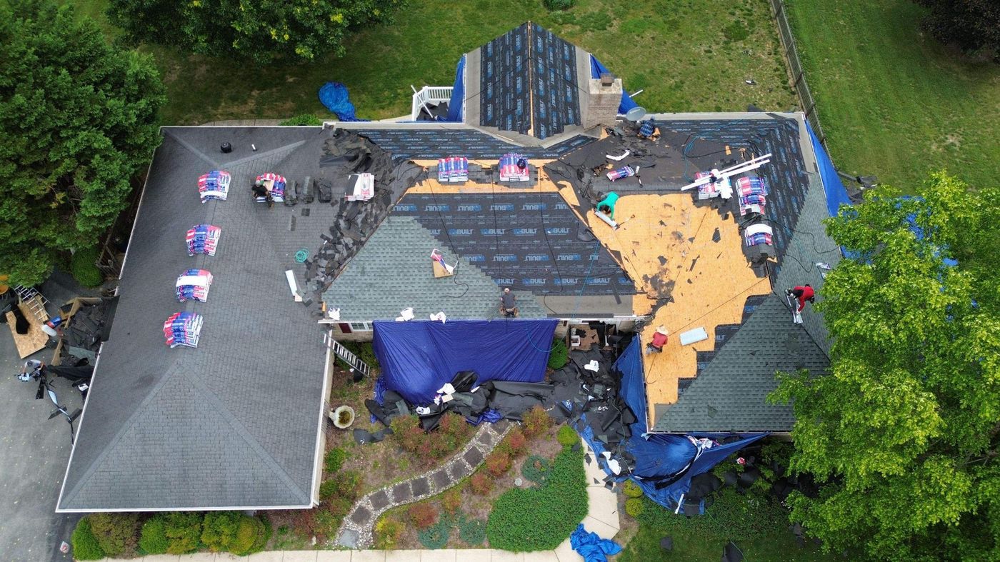 Aerial view of a roof tear-off in progress with tarps protecting the yard