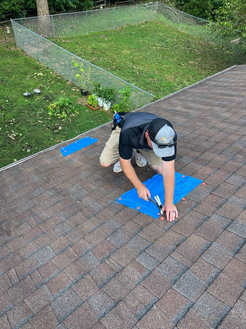 Roofer marking damaged shingles with blue tape during a storm inspection