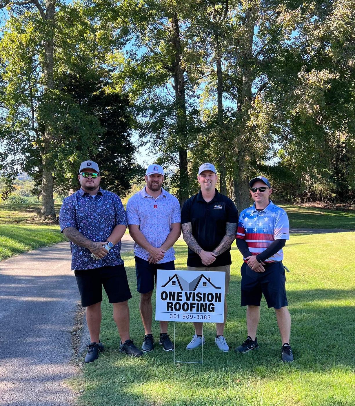 Four members of the One Vision Roofing team standing behind a company yard sign